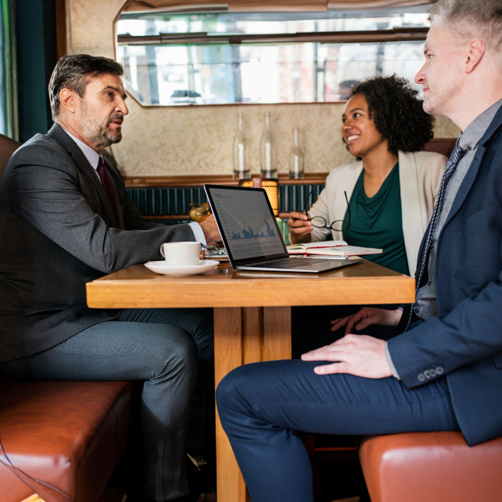 Three business people in formal attire discussing work in a cafe.